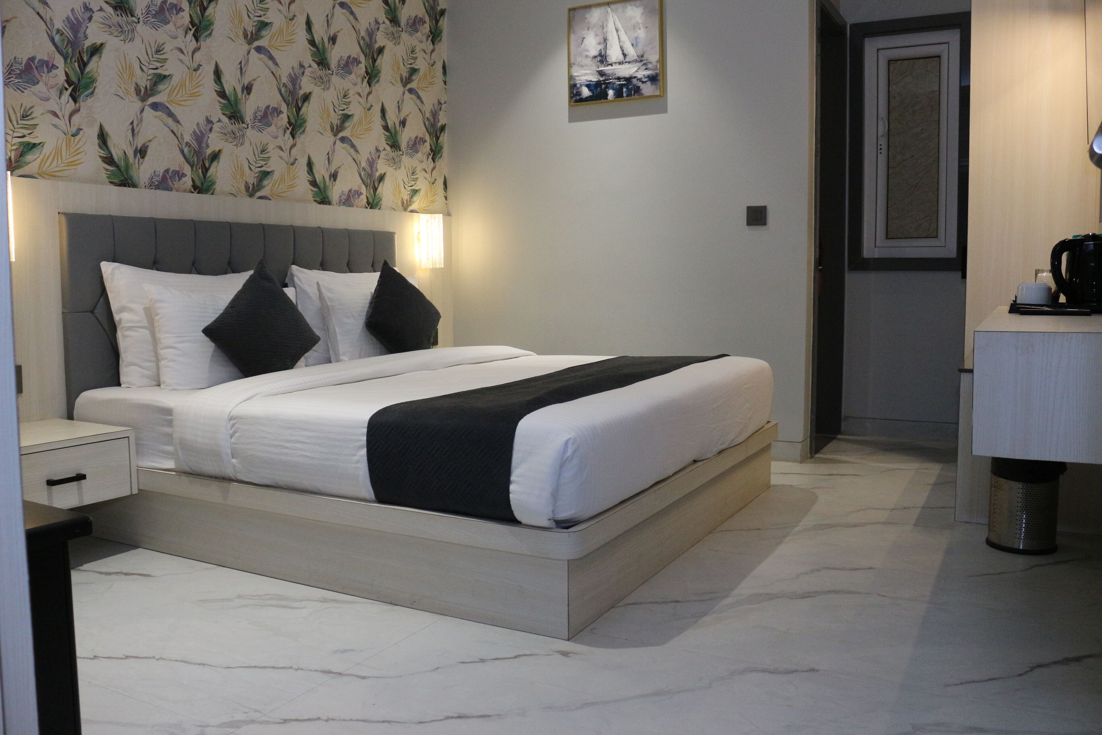 A neatly made bed with white and black bedding, a headboard with a light-colored panel, and a wall with a floral wallpaper pattern.