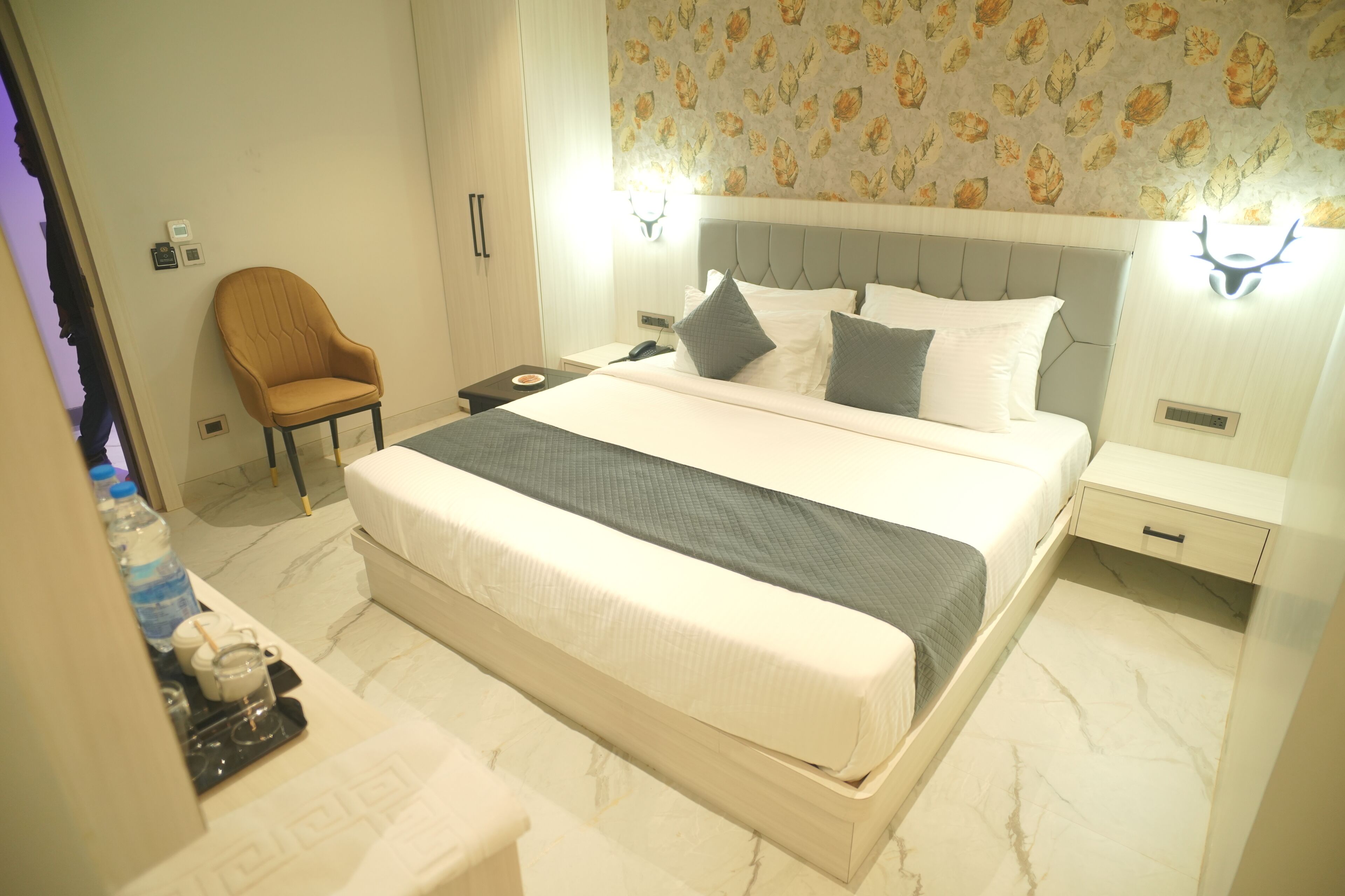 A neatly arranged hotel room with a large bed, a chair, a bedside table, and a nightstand.