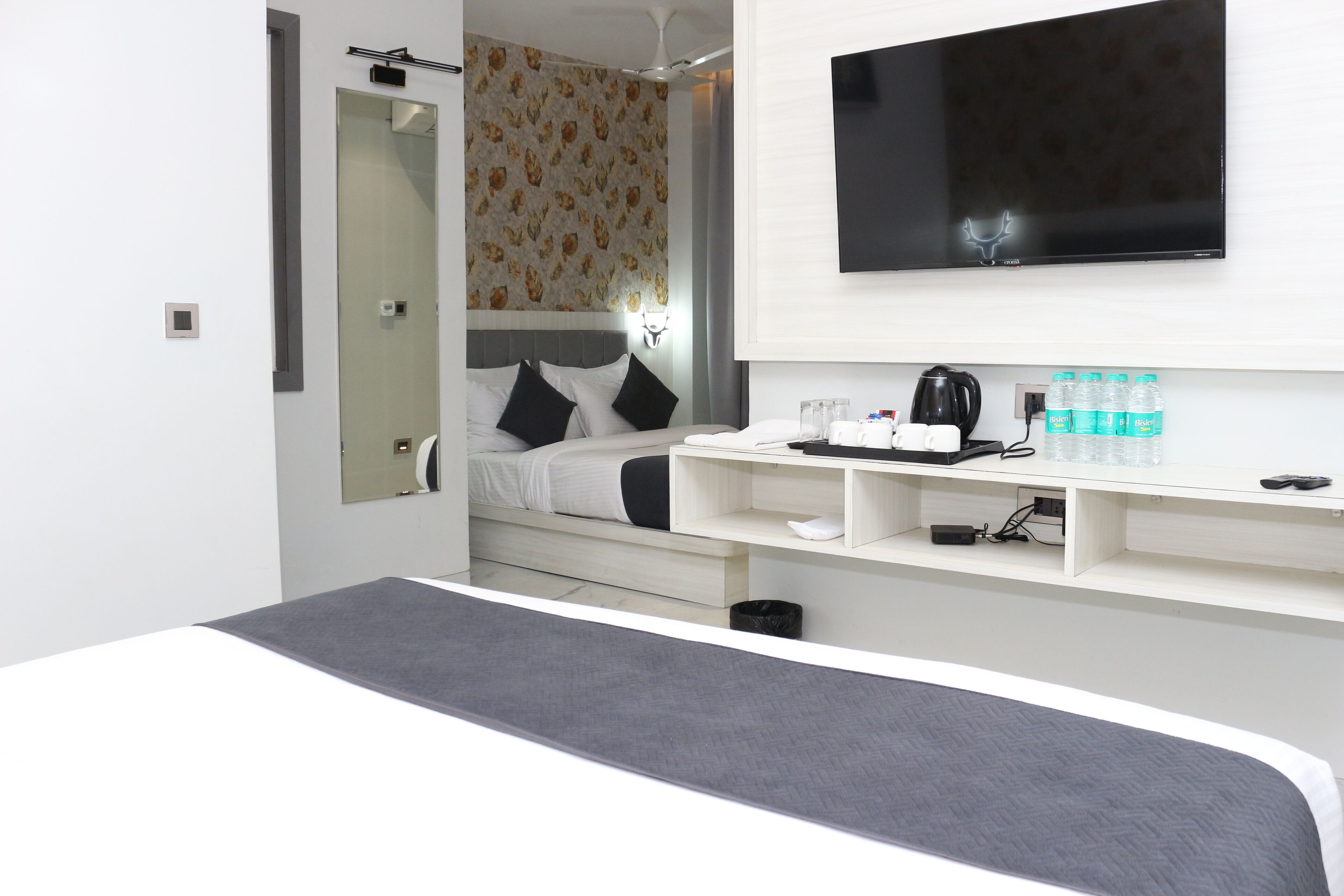 Quarto de hotel moderno com uma cama, TV fixada na parede, máquina de café e prateleira com artigos de higiene pessoal.