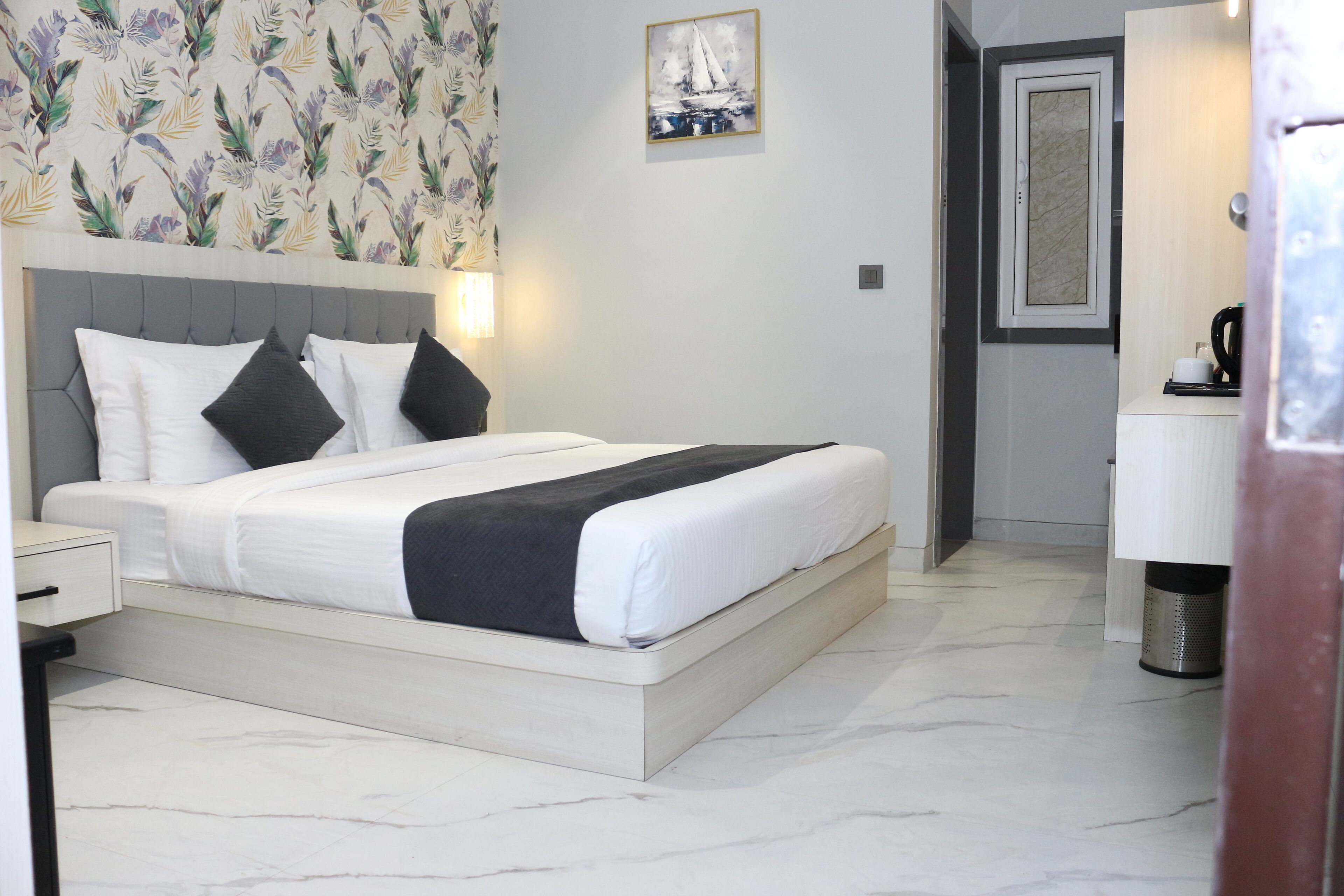 A neatly made bed with white and black bedding, a grey headboard, and a floral wallpaper pattern on the wall.