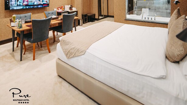 A hotel room with a large bed, a desk with chairs, a TV mounted on the wall, and a glass-enclosed shower area. - Pure Boutique Hotel  (Baku)