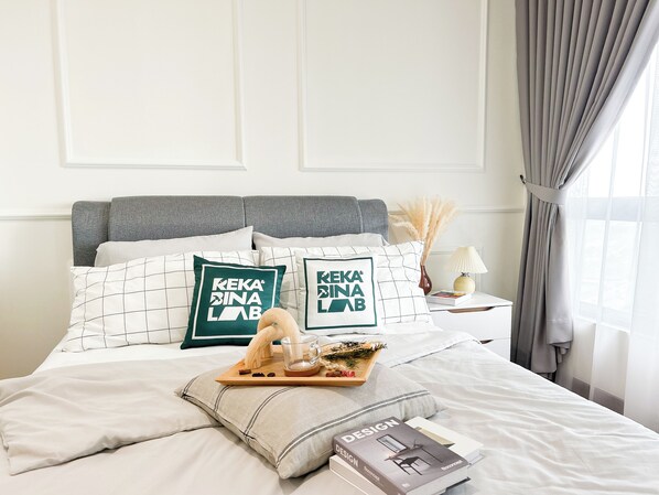 A neatly made bed with a book titled "DESIGN" and a tray with a glass and snacks.