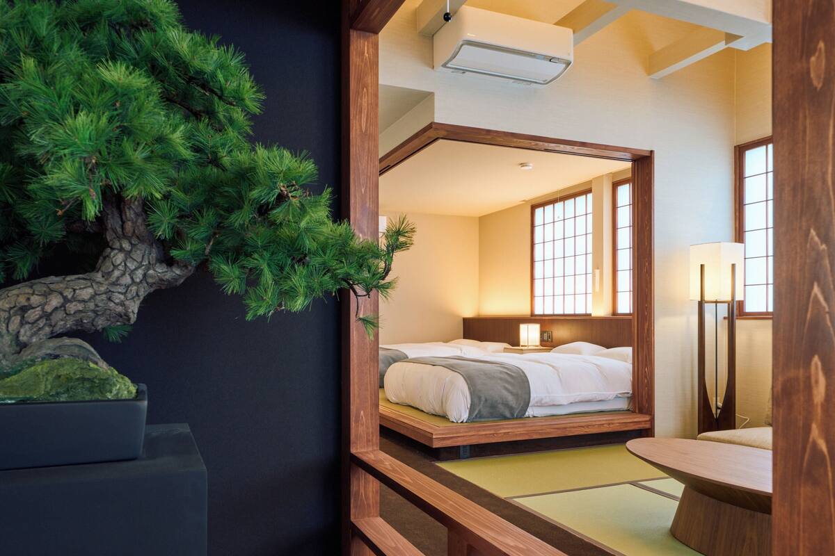 Une pièce de style japonais traditionnel, avec un sol recouvert de tatamis, un lit bas en bois, une petite table et une décoration représentant un pin.