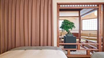 A room with a bed, a potted bonsai tree, a wooden partition, and a view of a traditional Japanese room.