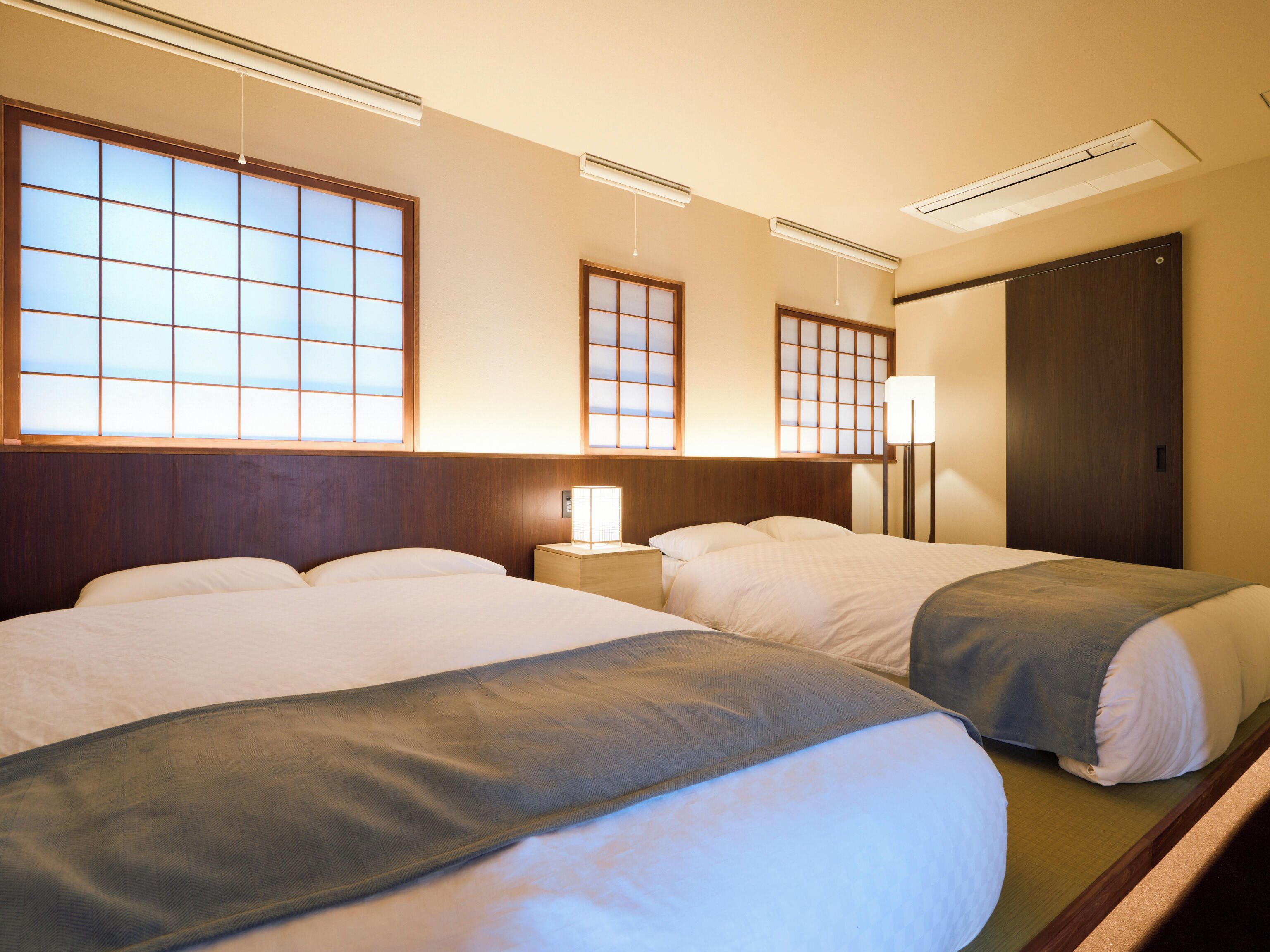 A hotel room with two beds, a nightstand with a lamp, and a wardrobe.
