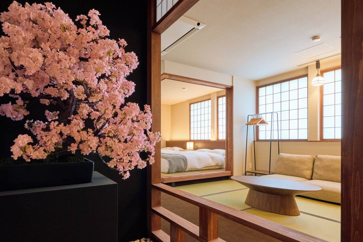Une pièce de style japonais traditionnel, avec un lit, un canapé et un grand cerisier en fleurs.