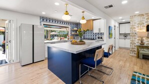 Une cuisine moderne dotée d’un îlot central, de luminaires suspendus et donnant sur l’espace extérieur.