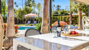 Un espace repas aménagé au bord de la piscine, avec une table dressée pour deux personnes, comprenant une bouteille de vin Bogle, un verre et une assiette de raisins.