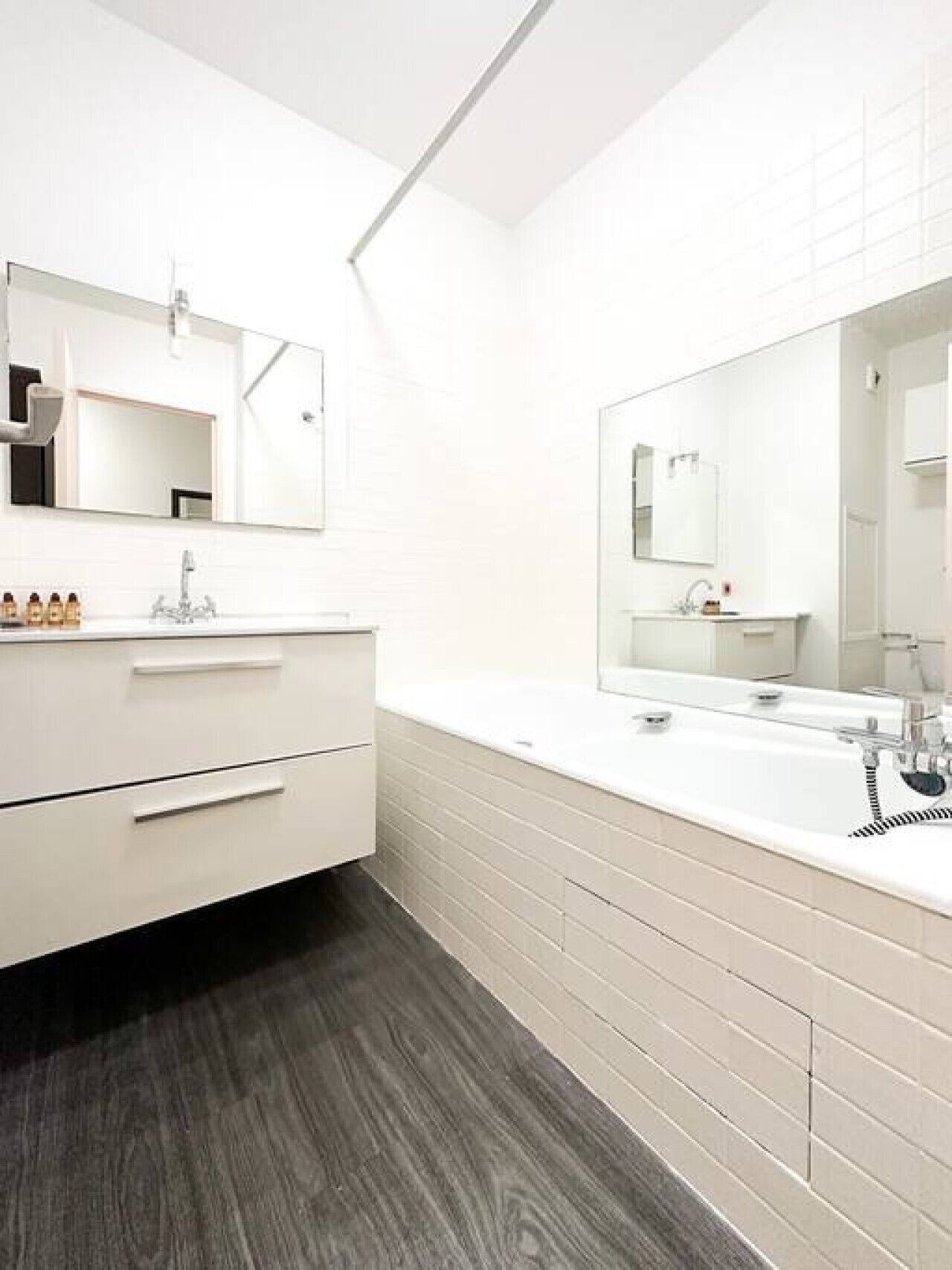 A modern bathroom with a white vanity, a large mirror, and a dark wooden floor.