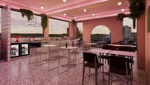 Un café moderne avec un intérieur rose, de grandes fenêtres et une vue sur le paysage urbain.
