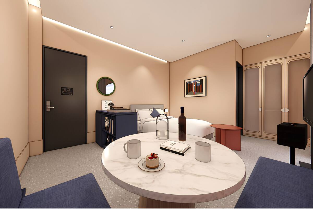Een moderne hotelkamer met een bed, nachtkastje, lamp en een ronde tafel met een taart en koffiekopjes.