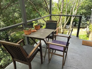 Une table en bois, des chaises et des plantes en pot sur un balcon donnant sur des arbres.