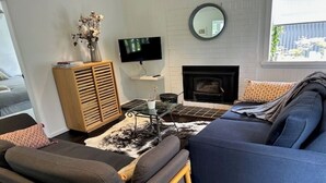 Een moderne woonkamer met een blauwe bank, een houten kast, een flatscreen televisie en een open haard.