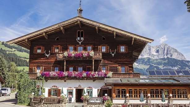 A wooden chalet with balconies, a stone foundation, and a mountain backdrop. - Ferienwohnung mit 1 Schlafzimmer fur 3 Personen (Reith bei Kitzbuehel)