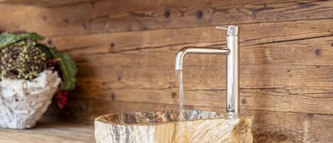 A rustic wooden wall with a metal faucet and a basin.