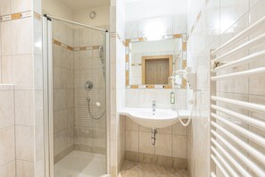 Ein modernes Badezimmer mit einer Glastrennwand-Dusche, einem Waschbecken mit Spiegel darüber und einem Handtuchhalter.