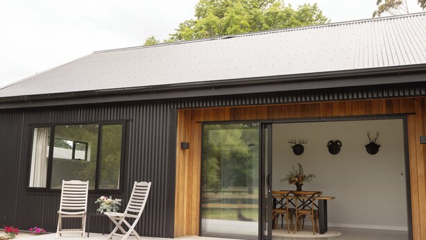Een modern gebouw met een grote glazen schuindeur, houten lambrisering en een eetgedeelte met een tafel en stoelen.