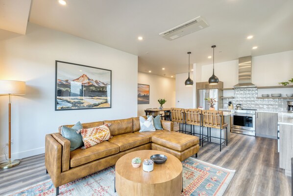 A modern living room with a leather sectional sofa, a round coffee table, and a dining area with bar stools.