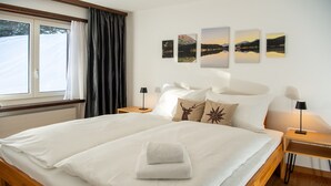 Ein Hotelzimmer mit einem großen Bett, zwei Nachttischen mit Lampen, einem Fenster mit Vorhängen und drei Landschaftsbildern an der Wand.