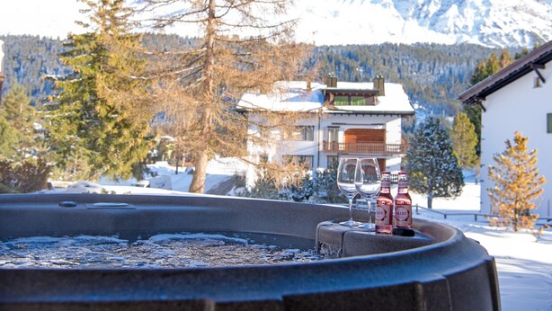 Ein Whirlpool mit zwei Flaschen Rotwein und einem Glas, umgeben von Schnee und Bergen.