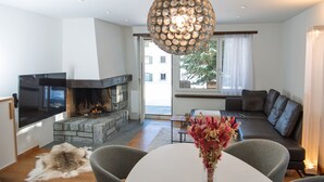 Ein modernes Wohnzimmer mit Kamin aus Stein, einem großen Flachbildfernseher, einer Couch und einem Essbereich mit Tisch und Stühlen.