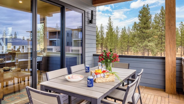En träveranda med ett bord dukat för middag, en vas med blommor och en utsikt över träd och byggnader i bakgrunden.