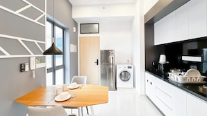 A modern kitchen with a built-in washing machine, a refrigerator, and a dining area with a table and chairs. - The Luxe by Manhattan Group  (Kuala Lumpur)