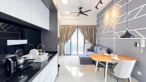 A modern kitchen with a black countertop, white cabinets, and a built-in oven. There is a dining area with a wooden table and white chairs. - The Luxe by Manhattan Group  (Kuala Lumpur)