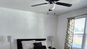 A bedroom with a large bed, a ceiling fan, a nightstand, a lamp, and a window with curtains. - OldCharm Spacious 2bdrmhouse in perfect location in Burley with WiFi,Central Air (Burley)