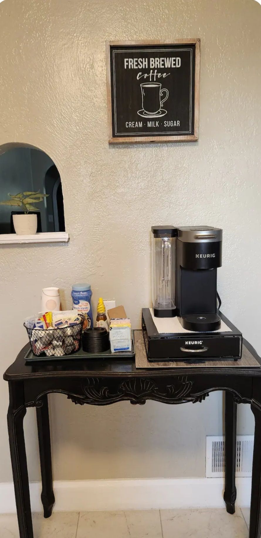 A coffee station with a Keurig coffee maker, a coffee pot, and various coffee-related items on a table.