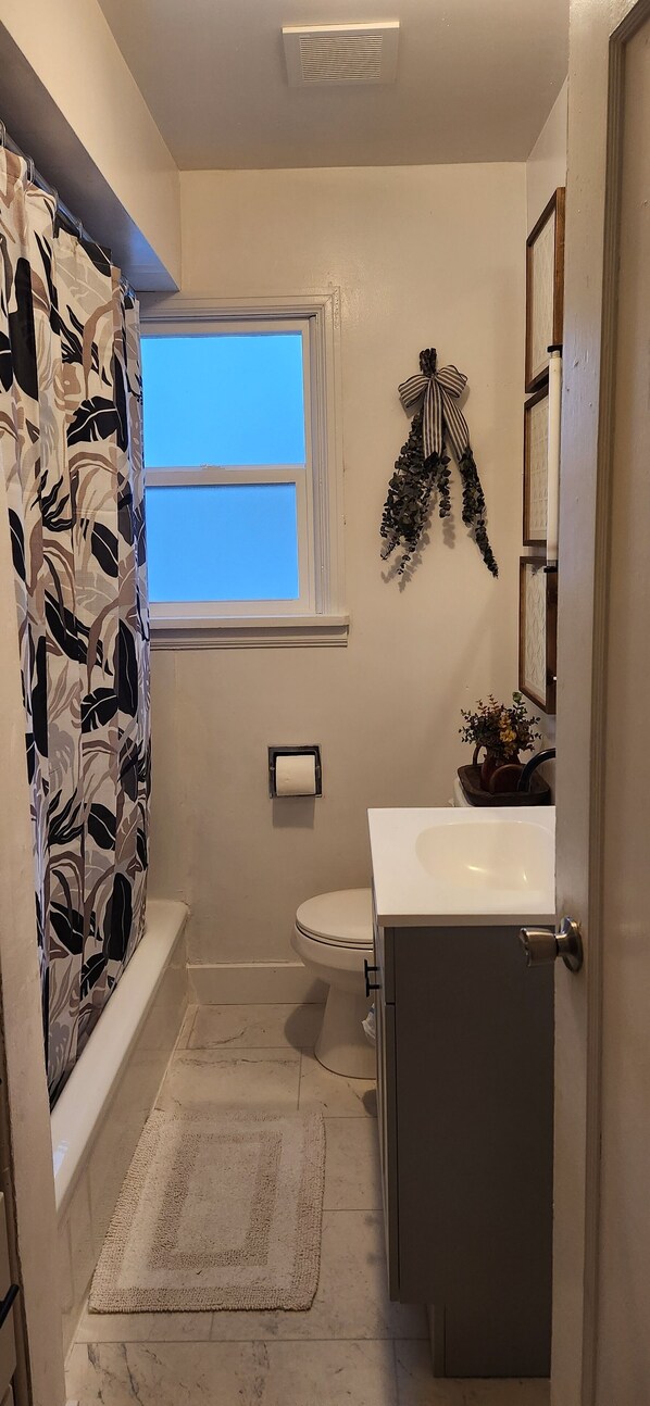 A bathroom with a shower curtain, a window, a toilet, a sink, and a mirror.