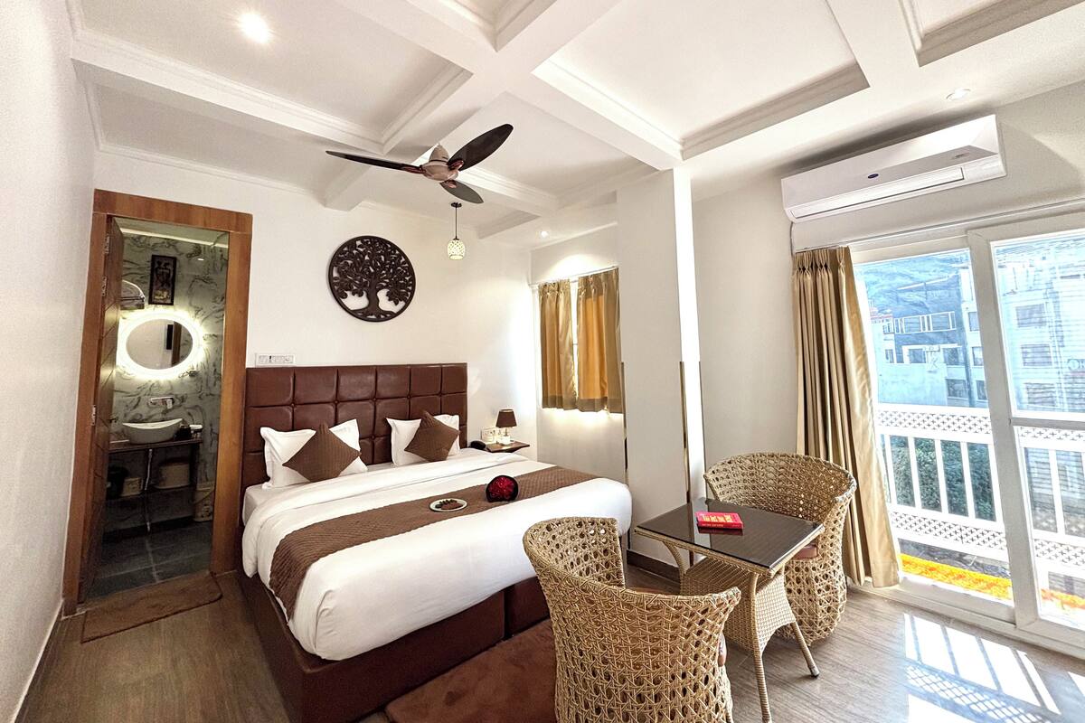 Ein Hotelzimmer mit einem Bett, einem runden Spiegel, einem Deckenventilator, einem kleinen Tisch mit Stühlen und einem Balkon mit Vorhängen.