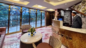 A hotel reception area with a marble floor, a reception desk, and a large window offering a city view. - Check Inn Homes - Rishikesh (Rishikesh)