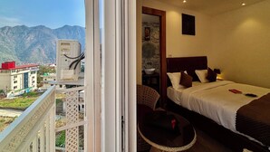 A hotel room with a bed, bedside table, and a view of mountains. - Check Inn Homes - Rishikesh (Rishikesh)