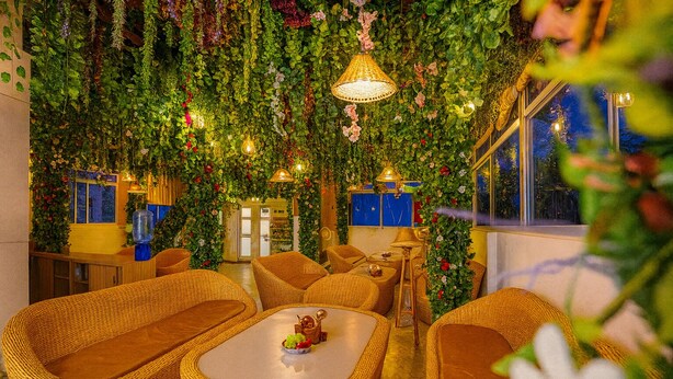 A cozy indoor seating area with wicker furniture, a central coffee table, and a wall adorned with greenery and hanging lights. - Check Inn Homes - Rishikesh (Rishikesh)