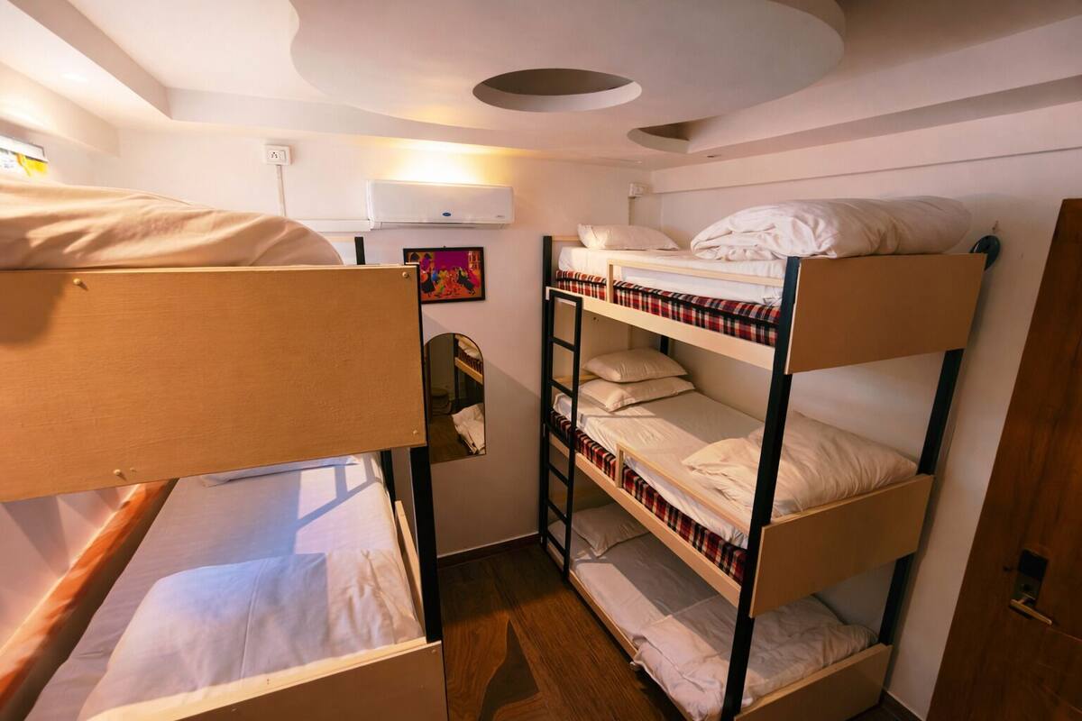 Ein Schlafsaalzimmer mit Etagenbetten, einem kleinen Spiegel, einer Klimaanlage und einer Tür.