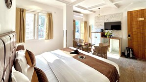 A hotel room with a bed, a ceiling fan, a TV, and a dining area with chairs. - Check Inn Homes - Rishikesh (Rishikesh)