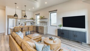 A modern kitchen with a dining area, a large TV, and a cozy seating area with a sofa and ottoman.