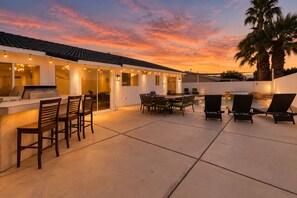 An outdoor patio area with a bar, seating, and a pool.