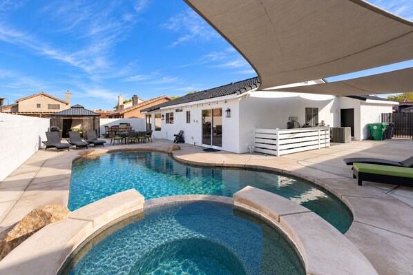 A swimming pool with a curved design, surrounded by a patio area with outdoor furniture.