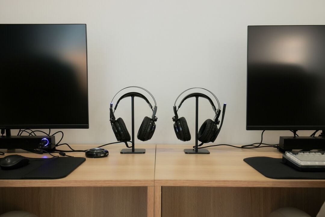 Ein Schreibtisch aus Holz mit zwei Monitoren, Kopfhörern auf Ständern, Maus und Tastatur.