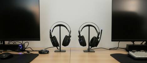 A dual-monitor setup with headphones on stands, a mouse, and a keyboard on a wooden desk.