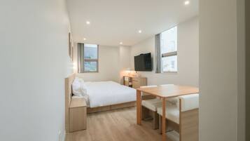A modern, compact room with a bed, a desk, and a TV.