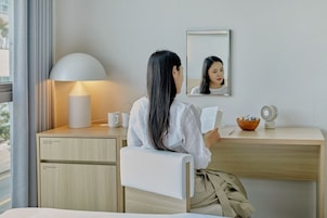 Habitación de hotel con escritorio, lámpara, espejo, ventilador y ventana con cortinas.