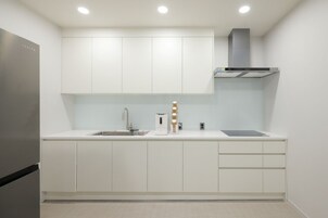 Una cocina moderna con armarios blancos, un refrigerador de acero inoxidable, un horno empotrado y una campana extractora.