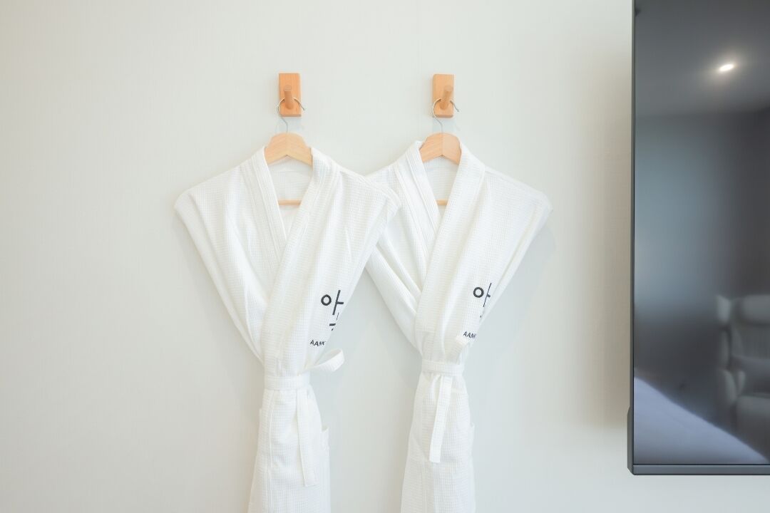 Two white robes hanging on wooden hangers against a plain wall.