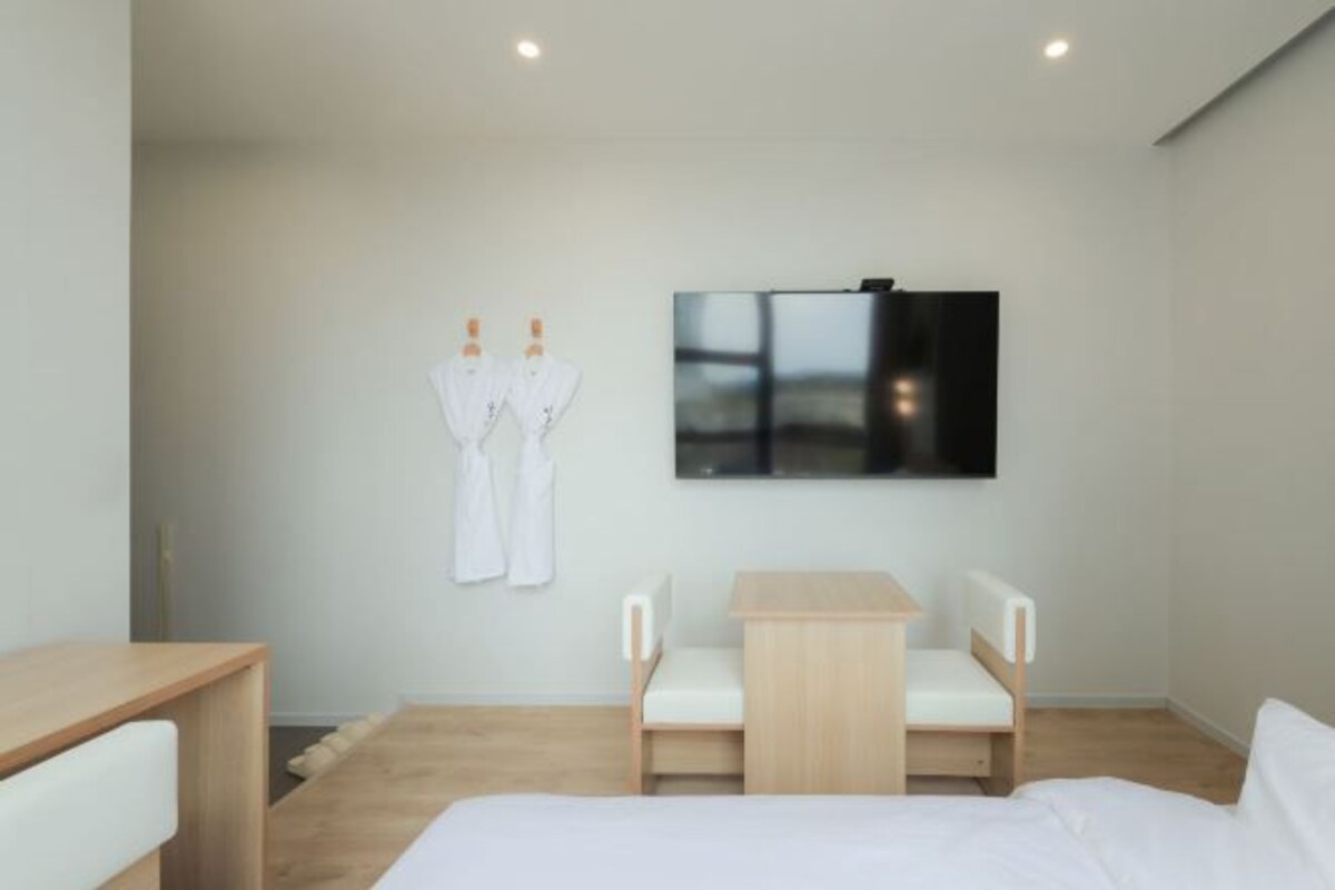 Ett modernt hotellrum med en säng, ett litet skrivbord, en stol och en tv som är monterad på väggen.