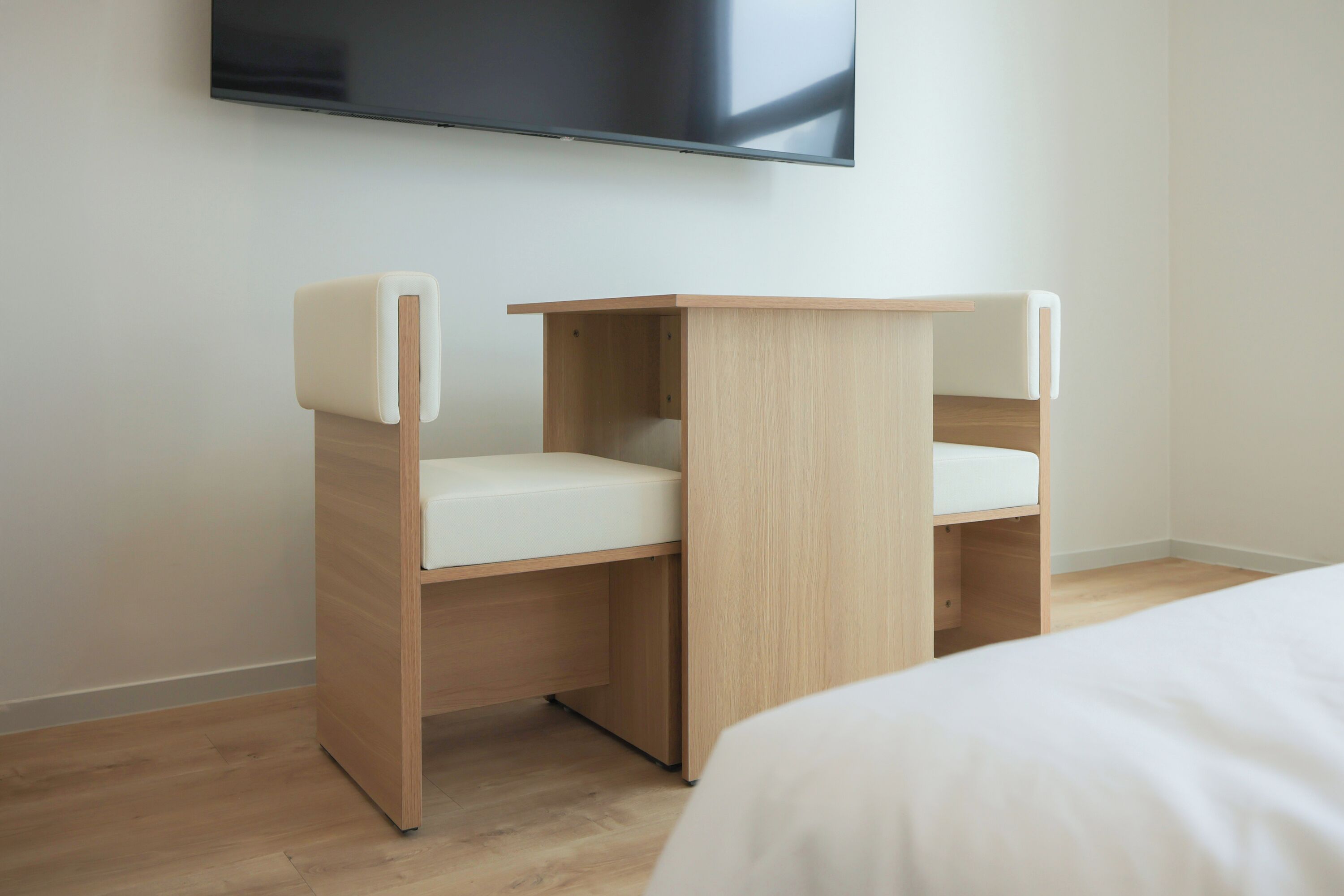 Una habitación moderna con una cama, un escritorio de madera con una silla blanca y un televisor de pantalla plana montado en la pared.