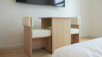 Una habitación moderna con una cama, un escritorio de madera con una silla blanca y un televisor de pantalla plana montado en la pared.