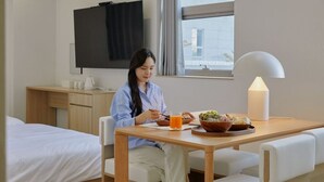 A hotel room with a bed, a desk with a flat-screen TV, a dining table with a lamp, and a window with curtains. - Anook Hotel Sejong (Sejong)